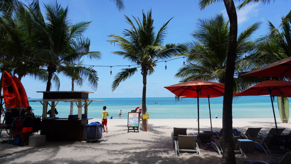 飯店前的熱帶海灘風景,棕櫚樹與陽傘下的旅人享受夏日悠閒
