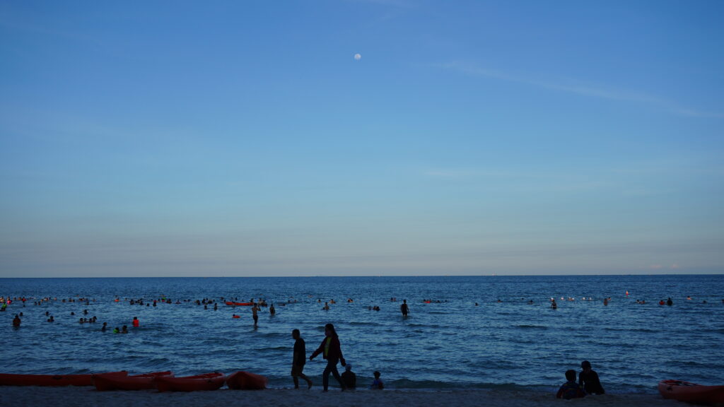 夕陽餘暉下的沙灘與人影,海浪輕拍岸邊的靜謐時光