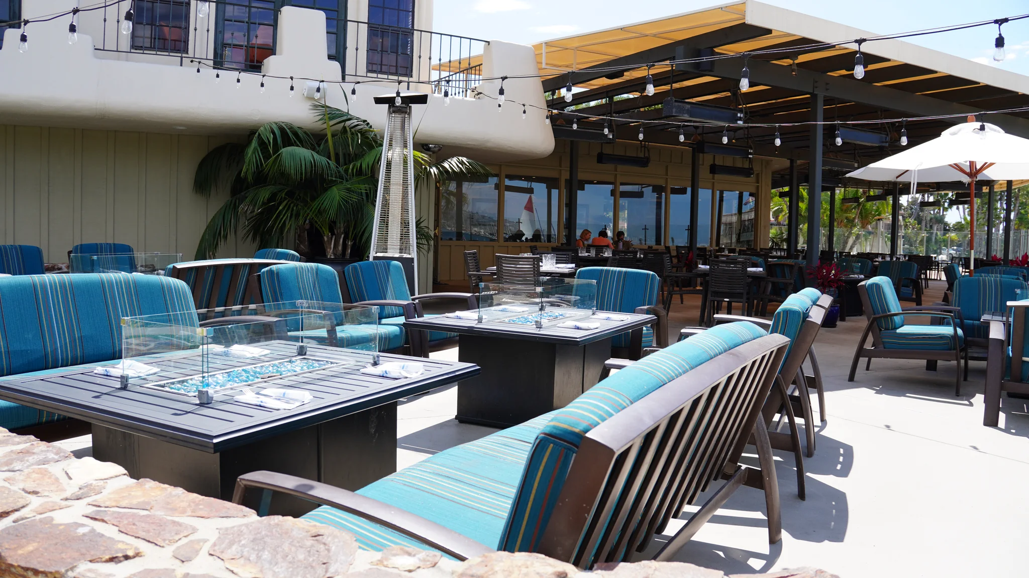 Bahia Resort Hotel 餐廳 Dockside 1953 的灣邊露台，玻璃防風罩的火爐桌與藍綠色條紋沙發座椅，後方是有遮陽棚的用餐區