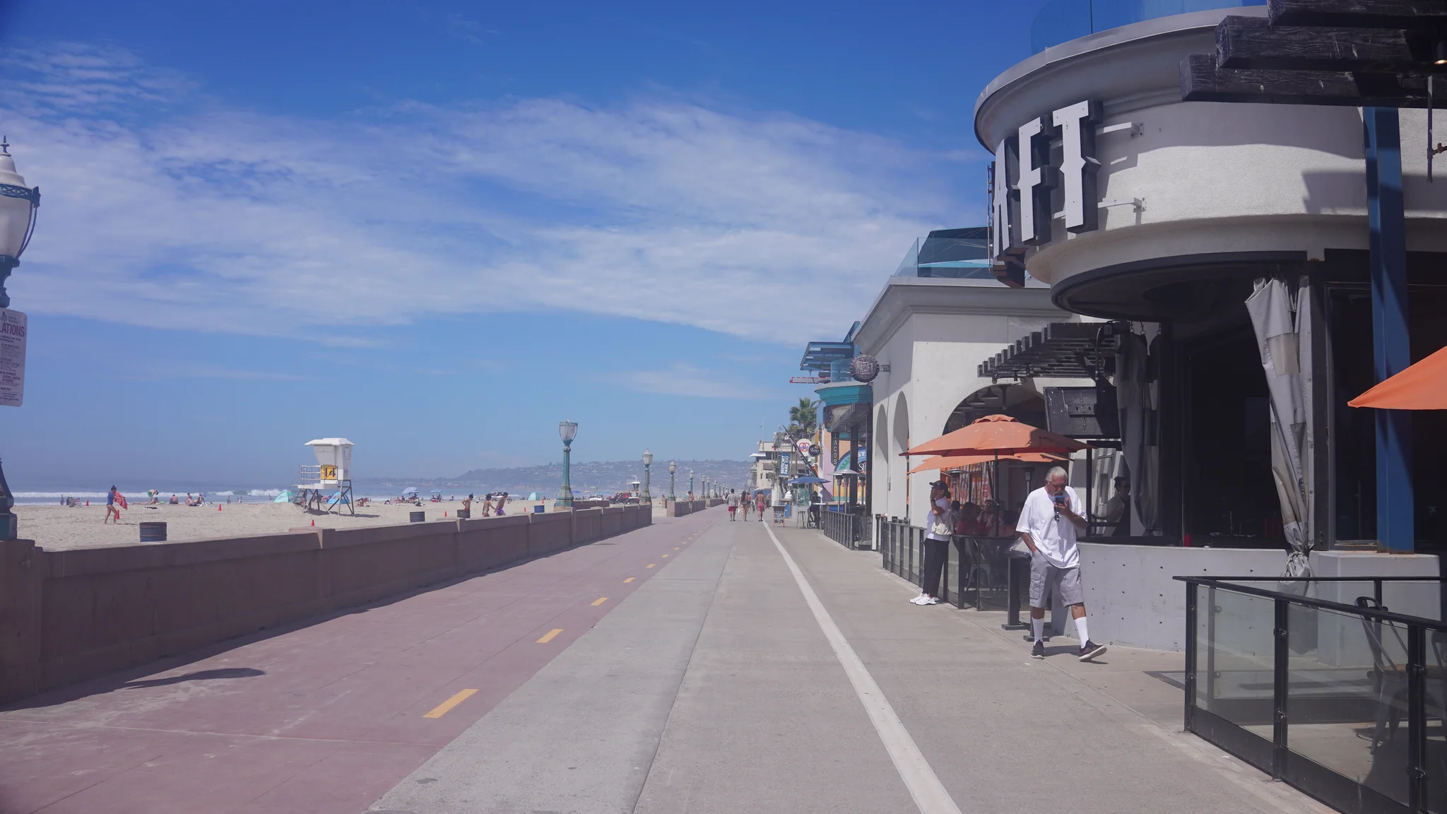 Mission Beach 濱海步道，左側是沙灘與救生塔，右側是餐廳的戶外座位與橘色遮陽傘